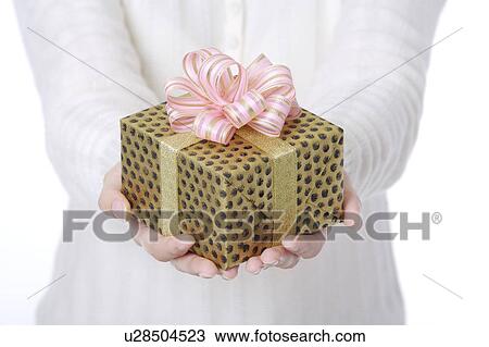Stock Image - Woman's hands holding a wrapped gift with beautiful packaging. Fotosearch