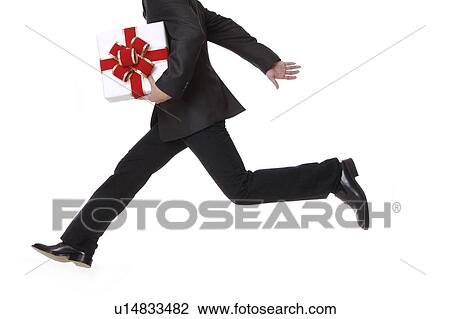Stock Image - Young man holding a wrapped gift and running. Fotosearch
