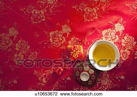 Stock Image - A cup of tea and Chinese decoration on red textile. Fotosearch