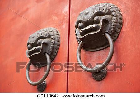 Stock Image - Close-up of two knocker of lion head shape on the red gate. Fotosearch