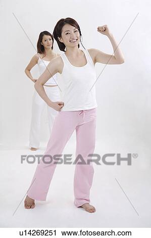 Stock Image - Young female coach exercising with young woman and smiling happily. Fotosearch