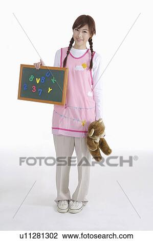 Stock Image - Young female teacher of kindergarten with teddy bear and little blackboard. Fotosearch