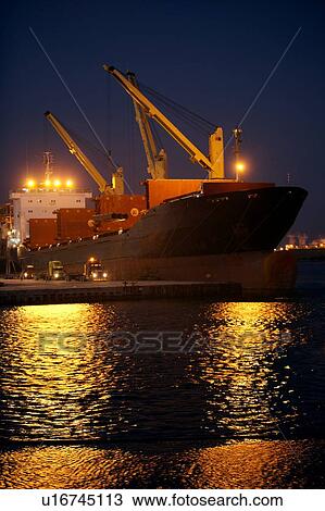 Stock Image - Offloading Pipe from Cargo Ship to Truck at Night. Fotosearch