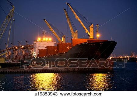Stock Image - Offloading Pipe from Cargo Ship to Truck at Dusk. Fotosearch