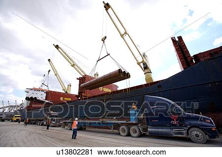 Stock Image - Offloading Pipe from Cargo Ship to Truck. Fotosearch