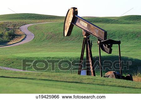 Stock Photograph - Pump Jack Operating Along Road in Green Hills. Fotosearch