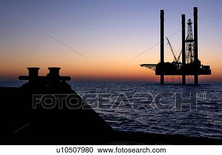 Stock Image - Silhouete View at Sunset of Offshore Oil Drilling Rig from Supply Boat. Fotosearch