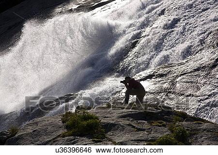 A photographer at a snow melt waterfall in Nordfjord, an arm of the larger Melfjord - situated just above the Arctic Circle - in northern Norway, Barents Sea. View Large Photo Image Stock Photograph - A photographer at a snow melt waterfall in Nordfjord, an arm of the larger Melfjord - situated just above the Arctic Circle - in northern Norway, Barents Sea.. Fotosearch