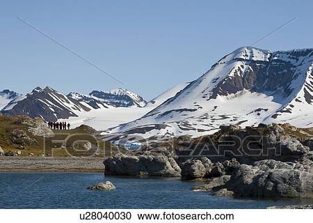 Stock Image - A view of hikers in front of the towering cliff and glacier in Hornsund (Horn Sound) on the southwestern side of Spitsbergen Island in the Svalbard Archipelago, Barents Sea, Norway.. Fotosearch
