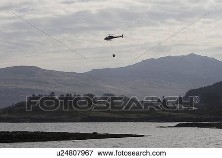 Stock Photo - Helicopter delivery of smolt (young salmon) from freshwater loch to salmon farm boat for trasnsfer to saltwater fishfarm pens. Hebrides, UK. Fotosearch