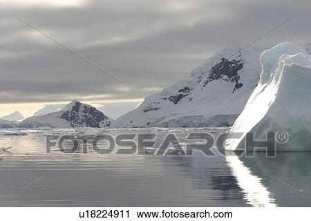Stock Image - Sunlight iceberg, against calm seas and moody skies Antarctica. Fotosearch