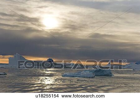 Sunset on snow-capped mountains and icebergs surrounded in brash ice in Crystal Sound near the Antarctic Circle on the west side of the Antarctic Peninsula. View Large Photo Image Picture - Sunset on snow-capped mountains and icebergs surrounded in brash ice in Crystal Sound near the Antarctic Circle on the west side of the Antarctic Peninsula.. Fotosearch