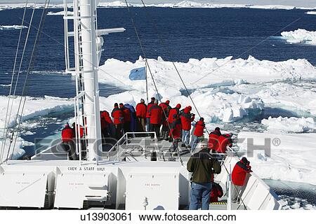 Stock Image - The National Geographic Endeavour breaking through ice floes in the Weddell Sea around the Antarctic Peninsula. Guests are on the bow watching the process.. Fotosearch