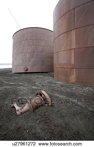 Stock Image - The old Norwegian whaling station at Whaler's Cove, Deception Island. The station ran from 1904 through 1931. Shown here are the old steel storage tanks for the rendered whale oil - note how they are beginning to tilt.. Fotosearch