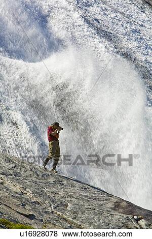 Stock Photo - A photographer at a snow melt waterfall in Nordfjord, an arm of the larger Melfjord - situated just above the Arctic Circle - in northern Norway, Barents Sea.. Fotosearch