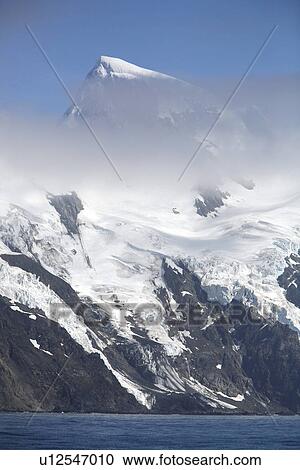 Stock Image - A view of the jagged peaks of Elephant Island shrouded in clouds in the South Shetland Island Group, Antarctica.. Fotosearch