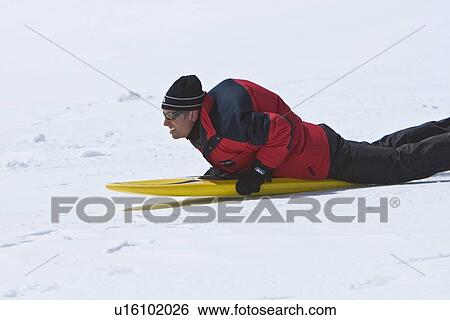 Stock Photograph - Lindblad Expeditions guests riding a snow board down a hill in Antarctica as part of expedition travel. NO MODEL RELEASES FOR THIS IMAGE.. Fotosearch