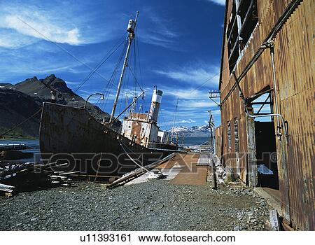 Stock Image - Remains of old whaling station with deserted buildings and boat in dock, Grytviken, South Georgia, sub Antarctic . Fotosearch