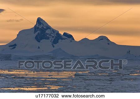 Stock Image - Sunset on snow-capped mountains and icebergs surrounded in brash ice in Crystal Sound near the Antarctic Circle on the west side of the Antarctic Peninsula.. Fotosearch