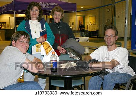 Stock Image - A man with physical disabilities sitting in his wheelchair at a table in a bar interacting with three friends.. Fotosearch