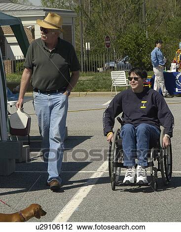 Stock Image - Man and woman (wheelchair user) tour a community fair. Fotosearch
