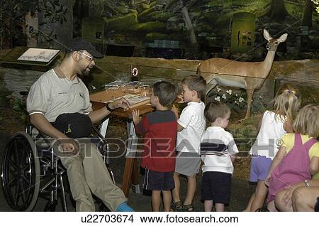 Man with a disability, utilizing a wheelchair for mobility, talking to a group of children at a museum exhibit. View Large Photo Image Picture - Man with a disability, utilizing a wheelchair for mobility, talking to a group of children at a museum exhibit.. Fotosearch