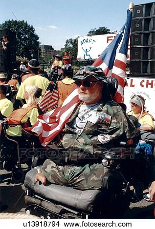 Picture - Man with a physical disability (missing lower limbs) who utilizes a wheelchair for mobility participating in a disability advocacy event with the U. S. Capitol in the background.. Fotosearch