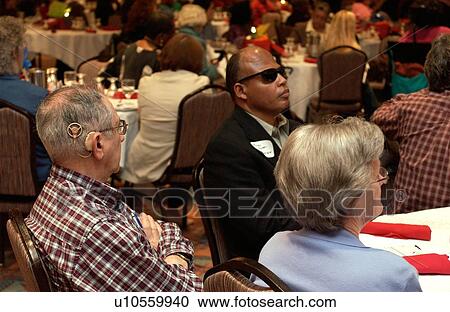 Stock Image - Man with a visual impairment and a man with a hearing impairment attending a conference for and about people with disabilities.. Fotosearch