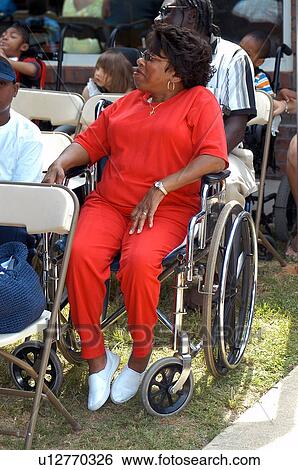 Stock Photograph - Proud grandma, who utilizes a wheelchair for mobility assistance, waiting for her granddaughter, who also has a disability, to graduate from preschool.. Fotosearch
