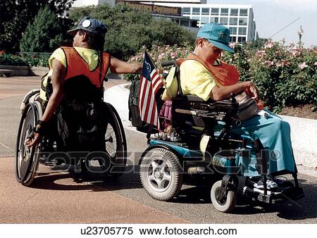 Stock Photography - Two men with disabilities, both using wheelchairs for mobility, heading their separate ways after a long day at a national disability advocacy event.. Fotosearch