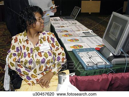 Stock Image - Woman with a disability, utilizing a wheelchair for mobility, checking out the latest innovations in assistive technology.. Fotosearch