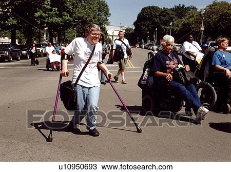Stock Image - Woman with a disability walking with the aid of crutches in Washington, D. C. along with other people with disabilities.. Fotosearch