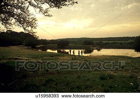 Stock Image - group of people standing by a pond in a field at sunset. Fotosearch