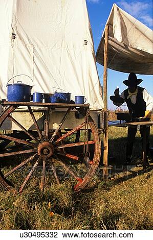 Stock Image - man cooking under a tent on the back of a wagon. Fotosearch