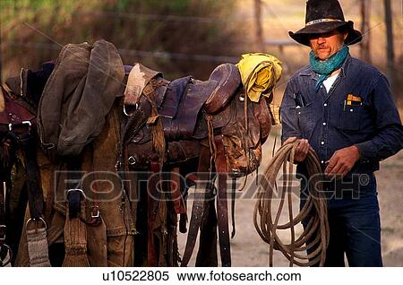 Stock Photography - man in a cowboy hat prepaing ropes and saddles. Fotosearch