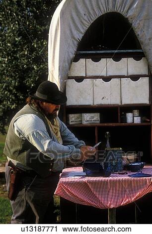 Stock Image - man preparing food on the back of a western covered wagon. Fotosearch