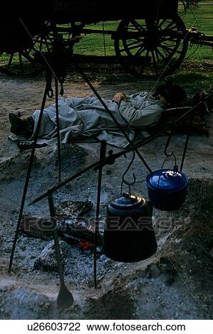 Stock Image - man sleeping beside a smoldering campfire. Fotosearch