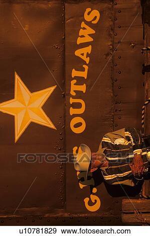 Stock Photo - older cowboy standing in front of a painted sign. Fotosearch