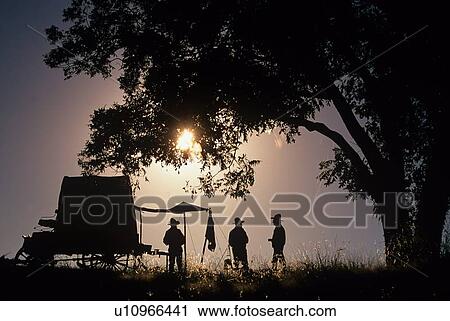 Stock Image - silhouette of three men preparing dinner on the trail. Fotosearch