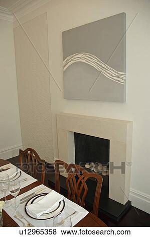 Stock Photo - Abstract painting above fireplace in modern dining room with white placemats and crockery on the table. Fotosearch