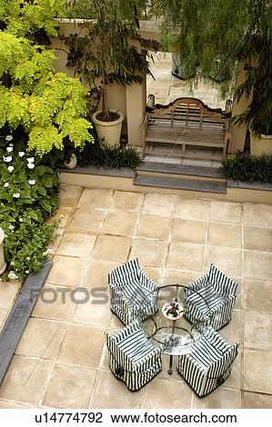 Aerial view of glass table and striped director's chairs on paved patio with ornate wooden bench in front of mirror on wall and acacia tree in the corner of the patio View Large Photo Image Stock Image - Aerial view of glass table and striped director's chairs on paved patio with ornate wooden bench in front of mirror on wall and acacia tree in the corner of the patio . Fotosearch