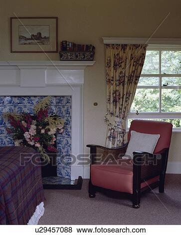 Stock Photo - Antique Bergere armchair in front of window with blue+white floral curtain in bedroom with white fireplace. Fotosearch