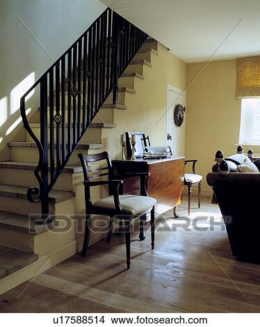 Antique chair and table in cream hall sitting room with wooden floor and staircase with black wrought iron bannister View Large Photo Image Picture - Antique chair and table in cream hall sitting room with wooden floor and staircase with black wrought iron bannister. Fotosearch
