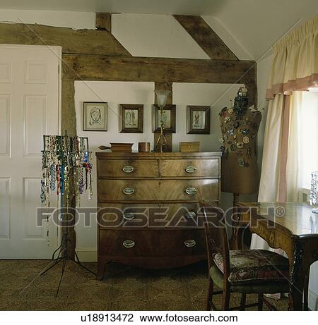Stock Image - Antique chest of drawers in beamed cottage bedroom with necklaces on stand. Fotosearch