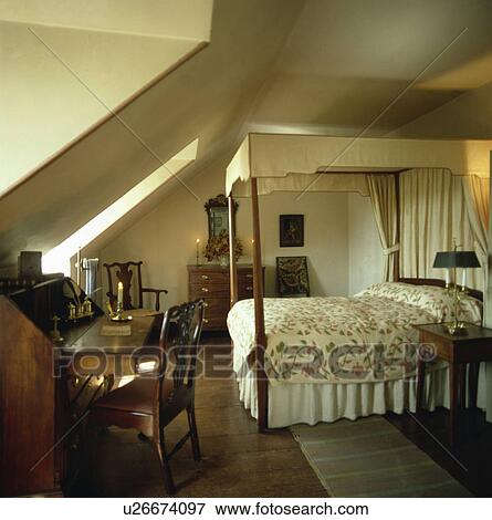 Antique desk and chair in attic bedroom with fourposter bed with cream drapes and floral patchwork quilt View Large Photo Image Stock Photo - Antique desk and chair in attic bedroom with fourposter bed with cream drapes and floral patchwork quilt. Fotosearch