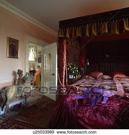 Stock Photo - Antique fourposter bed in country bedroom with pink velvet throw and oriental horse+rider figure. Fotosearch