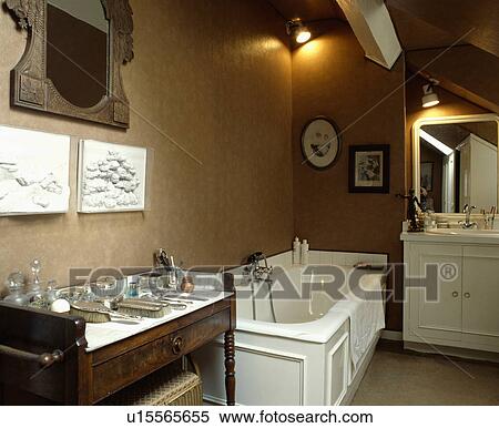 Stock Photography - Antique marble-topped washstand in pale brown bathroom with white bath and plaster plaques on wall. Fotosearch