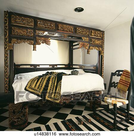 Antique oriental carved bed and chair in townhouse bedroom with striped rug on black and white floor View Large Photo Image Stock Photograph - Antique oriental carved bed and chair in townhouse bedroom with striped rug on black and white floor. Fotosearch