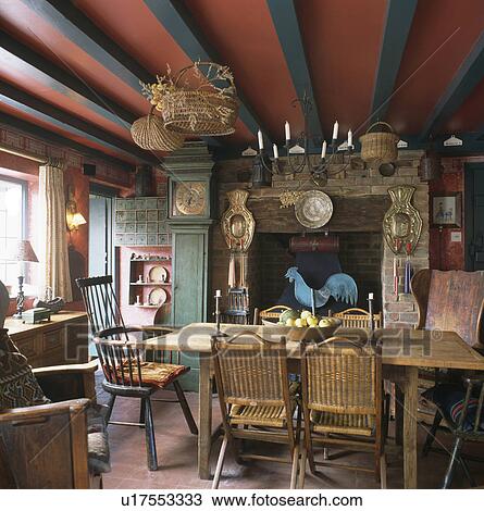 Stock Image - Antique table and chairs in diningroom with red ceiling and green beams and longcase clock beside fireplace. Fotosearch