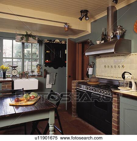 Stock Photography - Antique table with painted grey legs in grey country kitchen with black range oven. Fotosearch